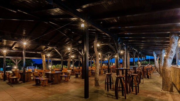 An outdoor restaurant with wooden tables and chairs, a covered roof, and trees. - Hostel Vagabundo (Novalja)