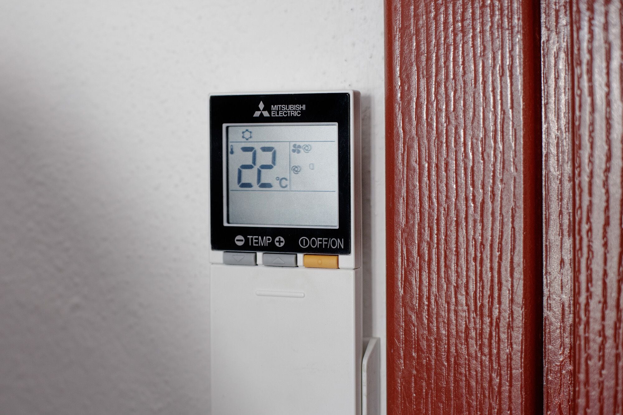 Termostato digital mostrando 22°C, con la marca Mitsubishi Electric, y un panel de control con ajuste de temperatura e interruptor de encendido.