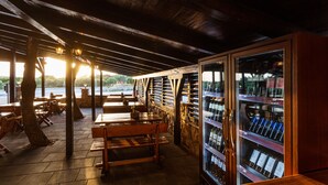 An outdoor seating area with wooden tables and benches, a stone wall, and a wine cooler with bottles. - Hostel Vagabundo (Novalja)