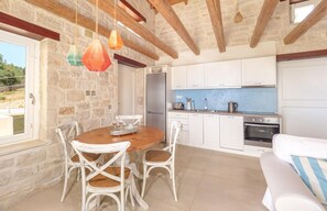 A cozy kitchen with white cabinets, a wooden dining table, and hanging pendant lights. - The Yiameli Collection - Meli (Zakynthos)