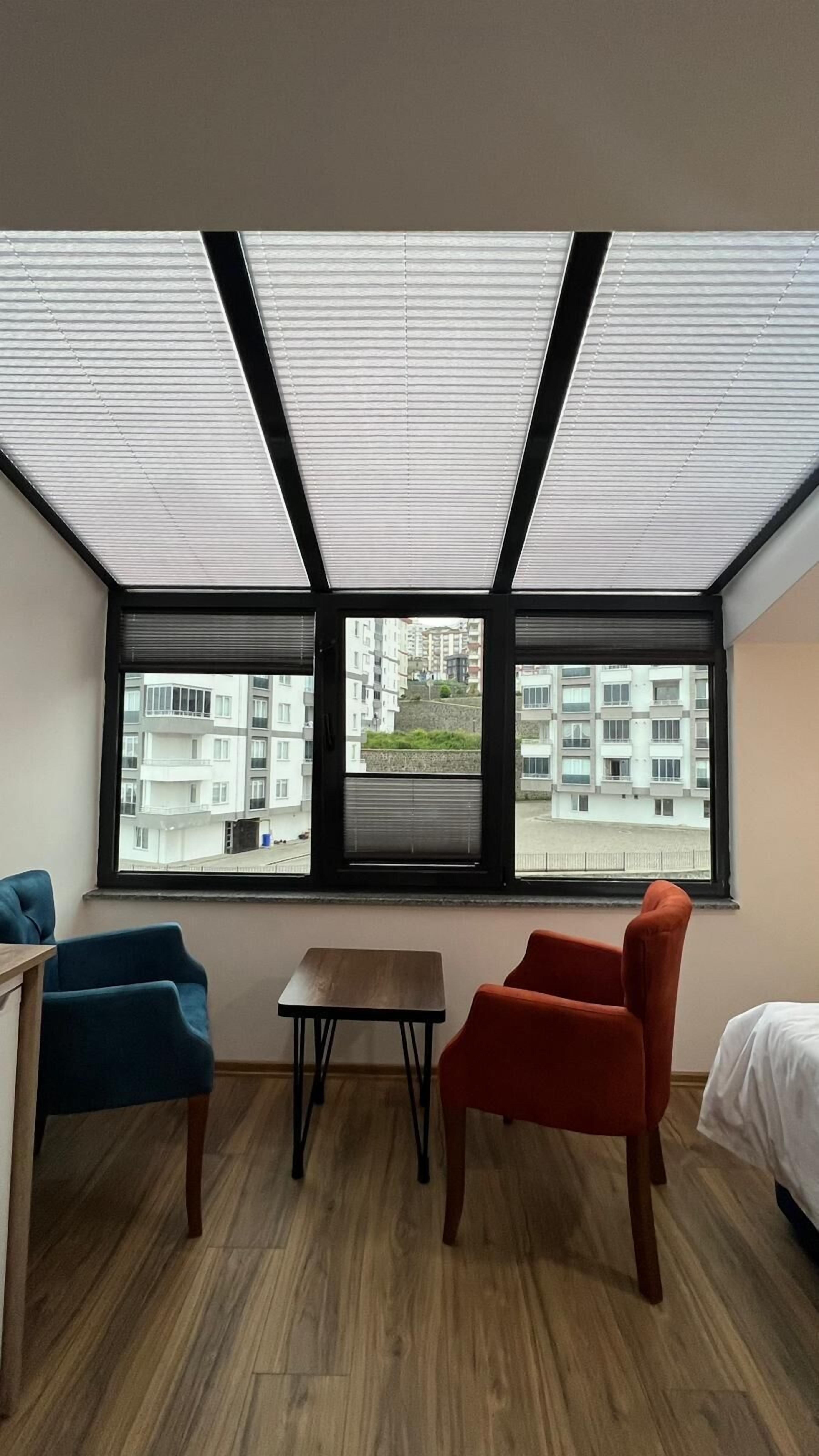Una habitación con un ventanal grande, una mesa de madera, dos sillas y una cama.