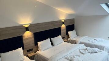 Habitación de hotel con tres camas, cada una con una toalla doblada.