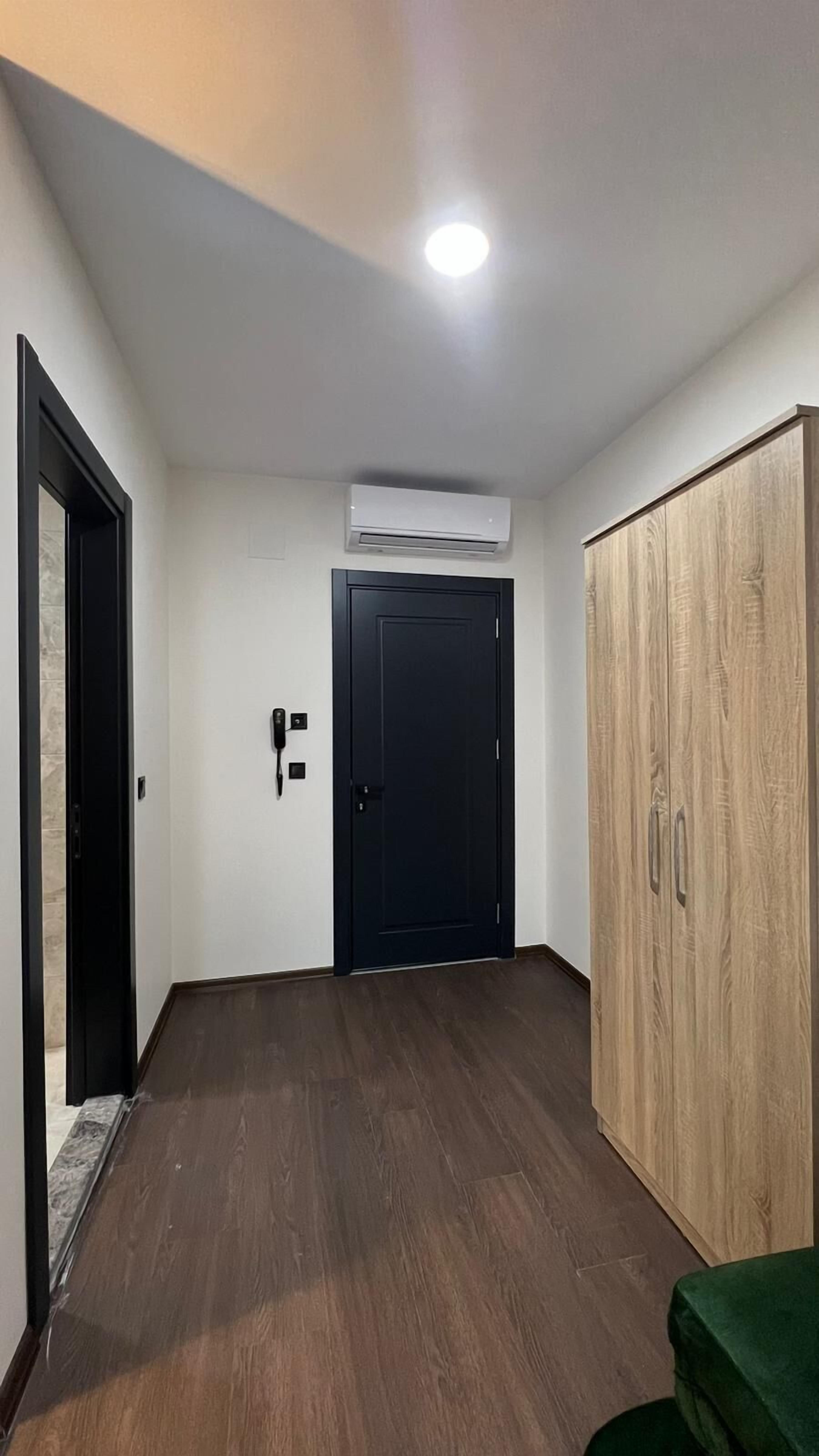 A room with a wooden wardrobe, a black door, and an air conditioning unit on the wall.