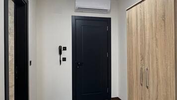 A room with a wooden wardrobe, a black door, and an air conditioning unit on the wall.