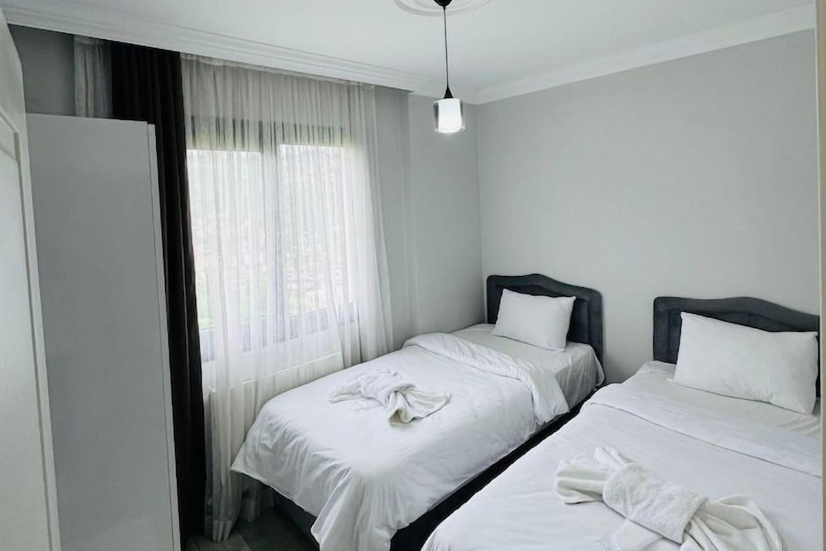 Habitación de hotel con dos camas, un armario, una ventana con cortinas traslúcidas y un equipo de aire acondicionado.