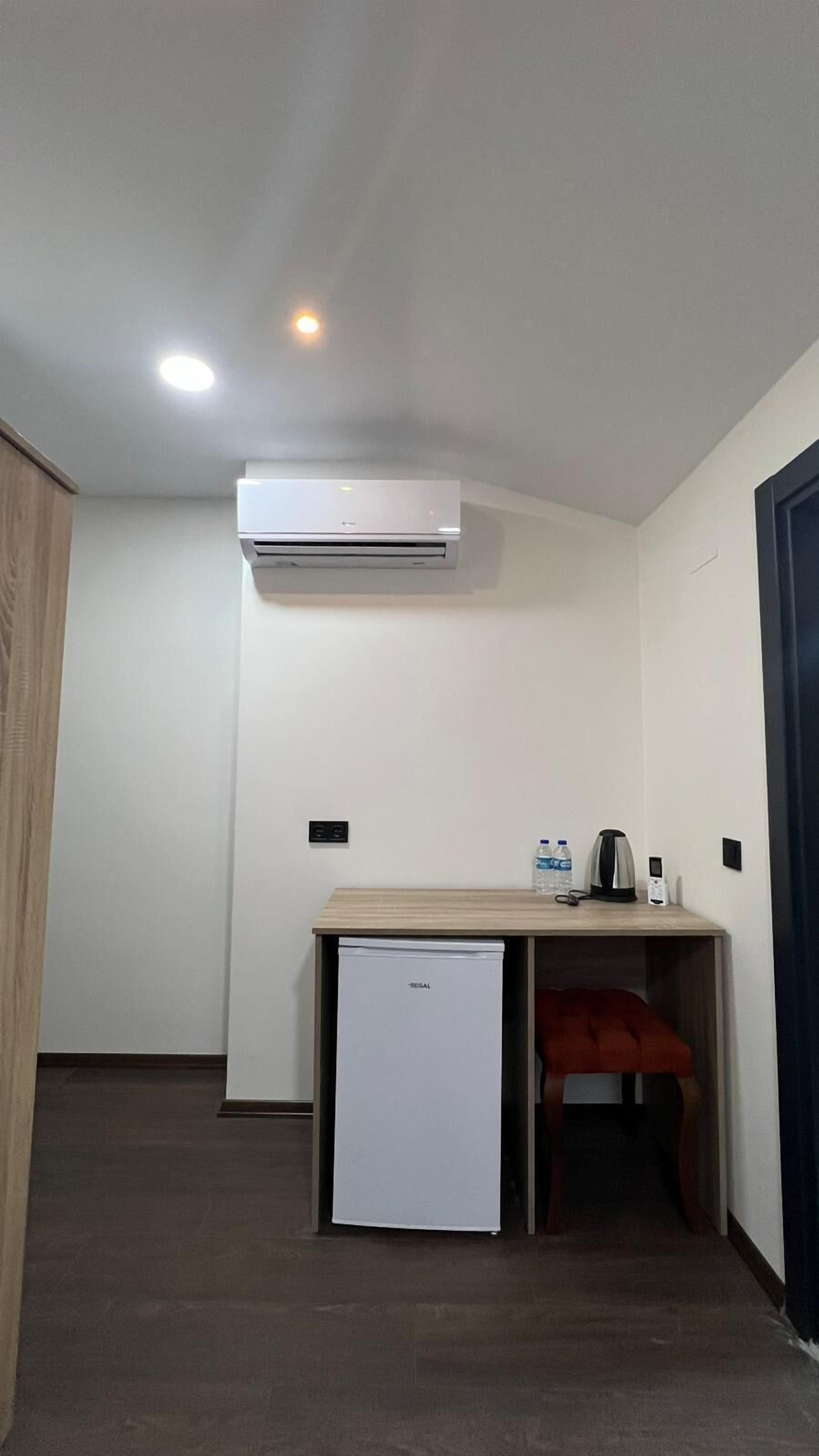 Una habitación compacta con kitchenette, un refrigerador pequeño y aire acondicionado instalado en el techo.