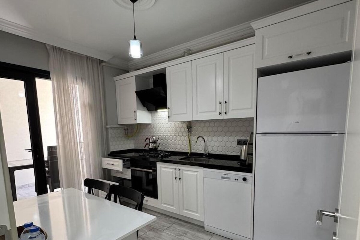 A modern kitchen with white cabinets, a black countertop, and a stainless steel refrigerator.