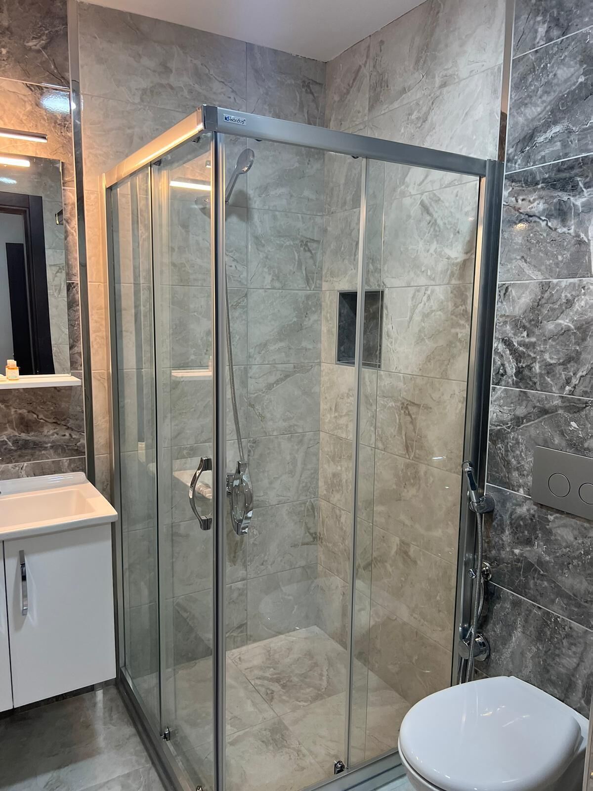A modern bathroom with a glass-enclosed shower, a white toilet, and a marble-tiled wall.