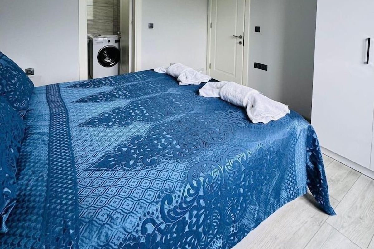 A bedroom with a bed, a washing machine, and a wardrobe.