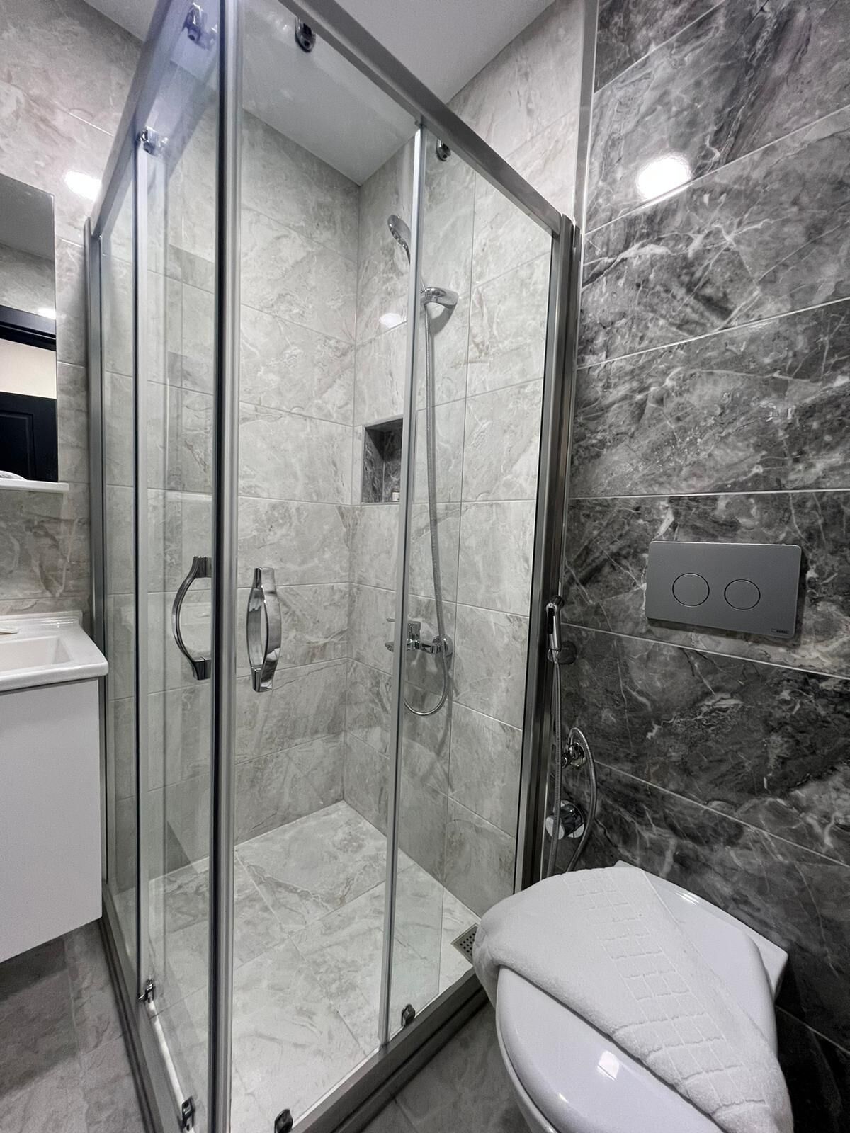 Un baño moderno con ducha de mampara de vidrio, inodoro blanco y pared de mármol.