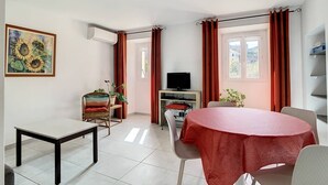 A room with a dining table, chairs, a television, and a window with curtains.