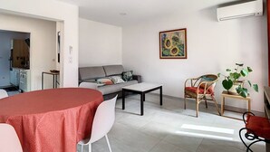 A modern living room with a dining table, sofa, and chairs. There is a painting on the wall and a potted plant.