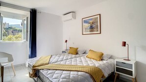 A bedroom with a large bed, two bedside tables, a chair, and a window with a view of greenery.