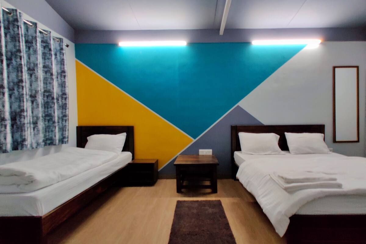 Une chambre d’hôtel avec deux lits simples, une table de chevet et un mur orné d  ’un motif géométrique.