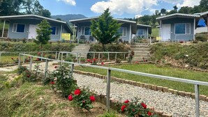 A row of small, single-story cabins with a gravel pathway and red flowers in the foreground. - KedaraYatih Resort (Ukhimath)
