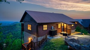 A log cabin with a metal roof, a porch, and a view of the surrounding forest. - TopOfTheMountain, Fully Paved Roads, PoolTable, HotTub, VideoGames,EV Charger (Sevierville)