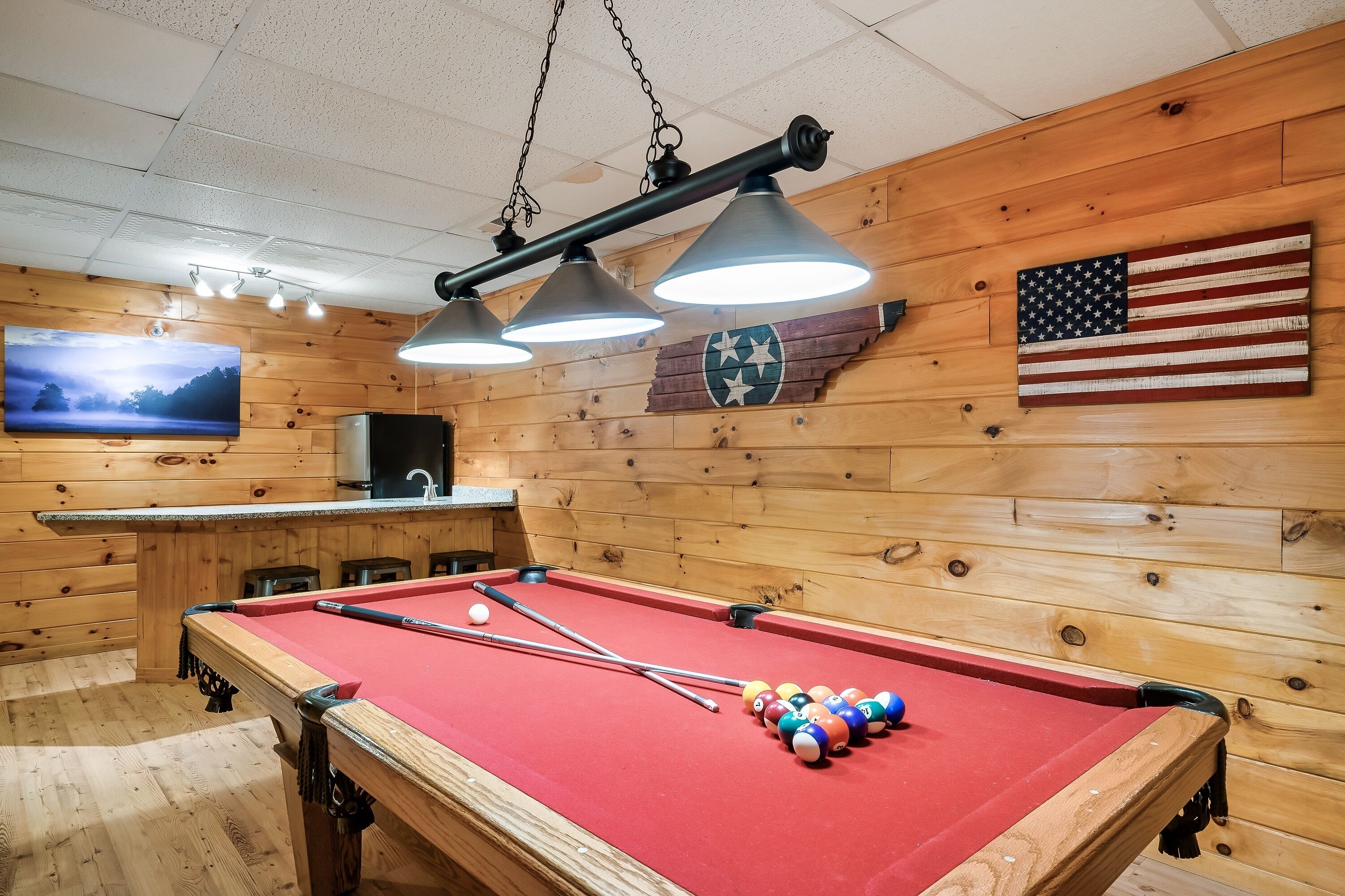 Ein Billardtisch mit Kugeln, ein Fernseher und eine amerikanische Flagge an einer Holzwand.
