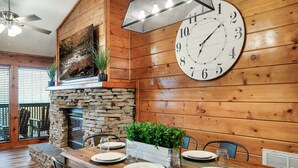 A wooden dining area with a stone fireplace, a large clock, and a plant centerpiece. - TopOfTheMountain, Fully Paved Roads, PoolTable, HotTub, VideoGames,EV Charger (Sevierville)