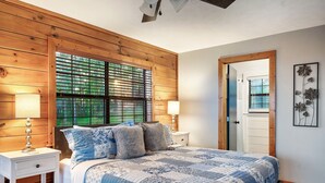 A bedroom with a wooden headboard, a large bed with a blue and white quilt, two bedside tables with lamps, and a wooden door. - TopOfTheMountain, Fully Paved Roads, PoolTable, HotTub, VideoGames,EV Charger (Sevierville)