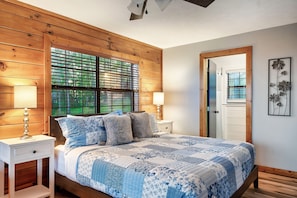 A bedroom with a wooden headboard, a large bed with a blue and white quilt, two bedside tables with lamps, and a wooden door. - TopOfTheMountain, Fully Paved Roads, PoolTable, HotTub, VideoGames,EV Charger (Sevierville)