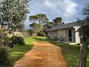 A residential property with a dirt driveway leading to a house with a porch.