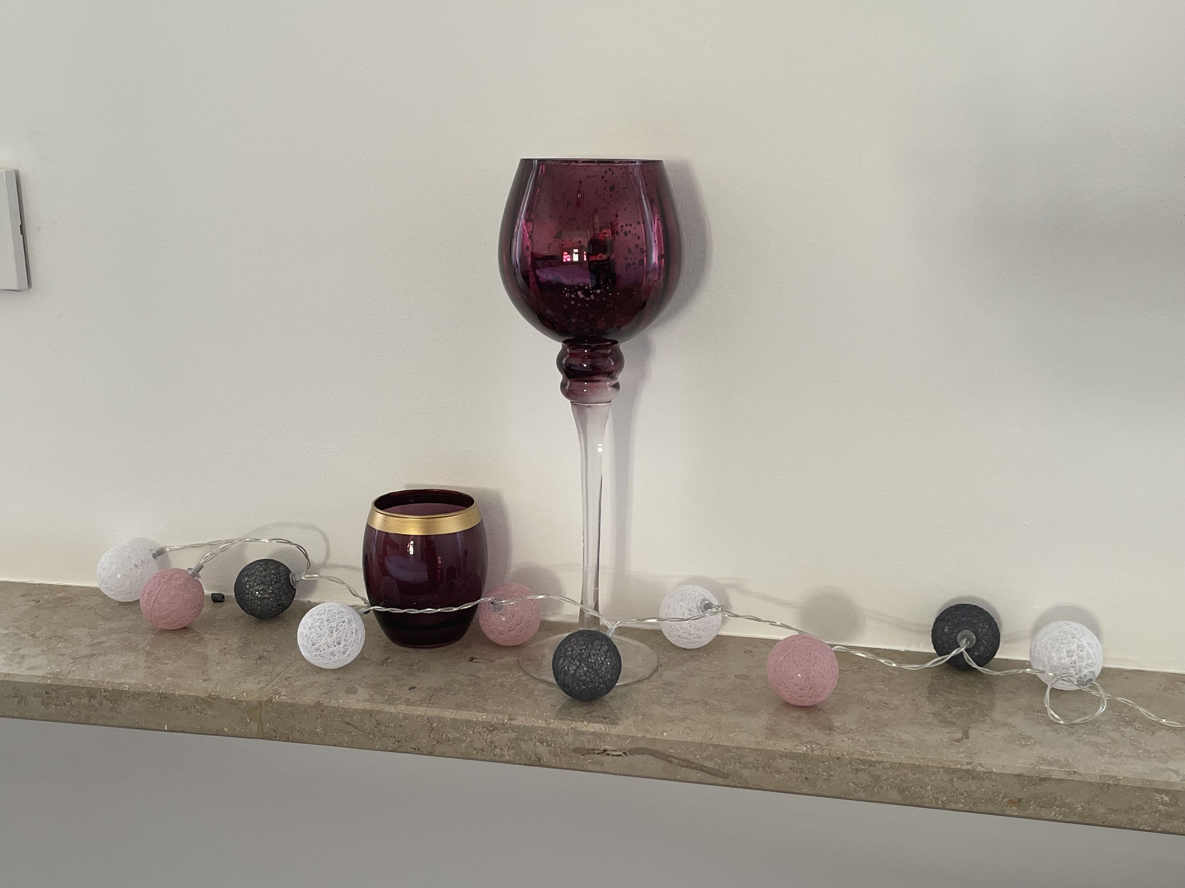 Een wijnglas, een kaars en decoratieve lampjes op een plank.