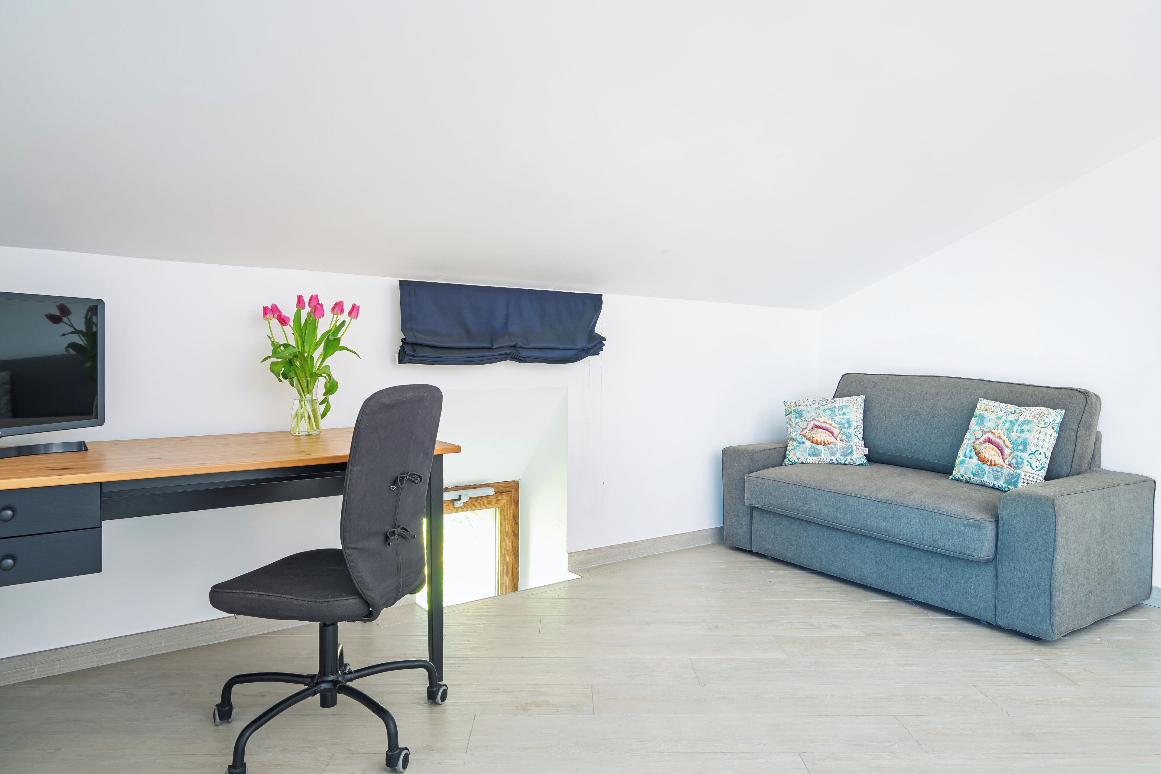 Et moderne værelse med skrivebord, stol og en grå sofa med dekorative puder.