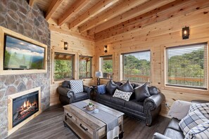Relax in a warm living room with a fireplace, comfortable seating, and scenic views of the surrounding greenery.