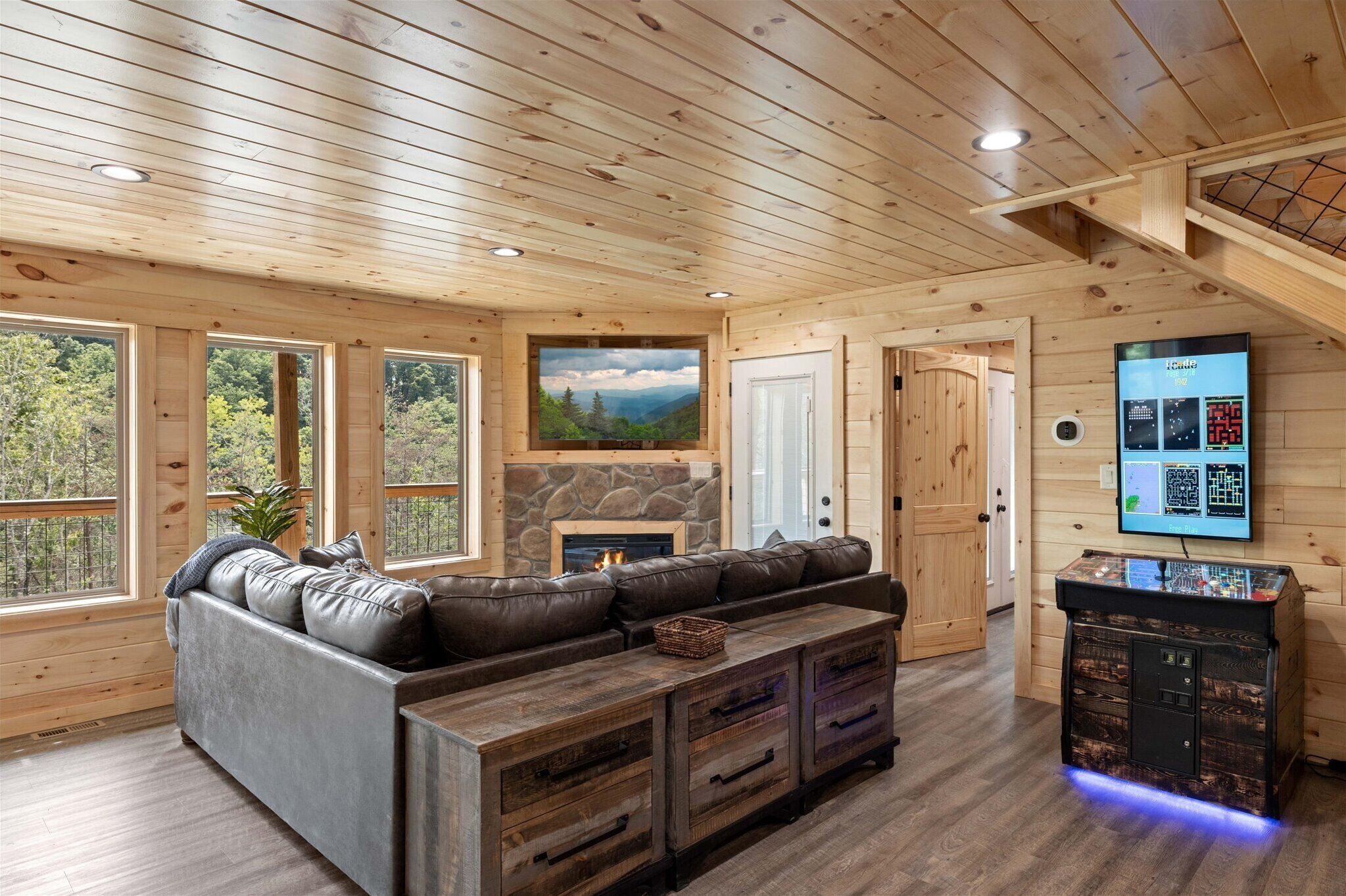 L’intérieur d’un chalet en bois est doté d’une cheminée en pierre, d’un canapé en cuir et d’un téléviseur fixé au mur.