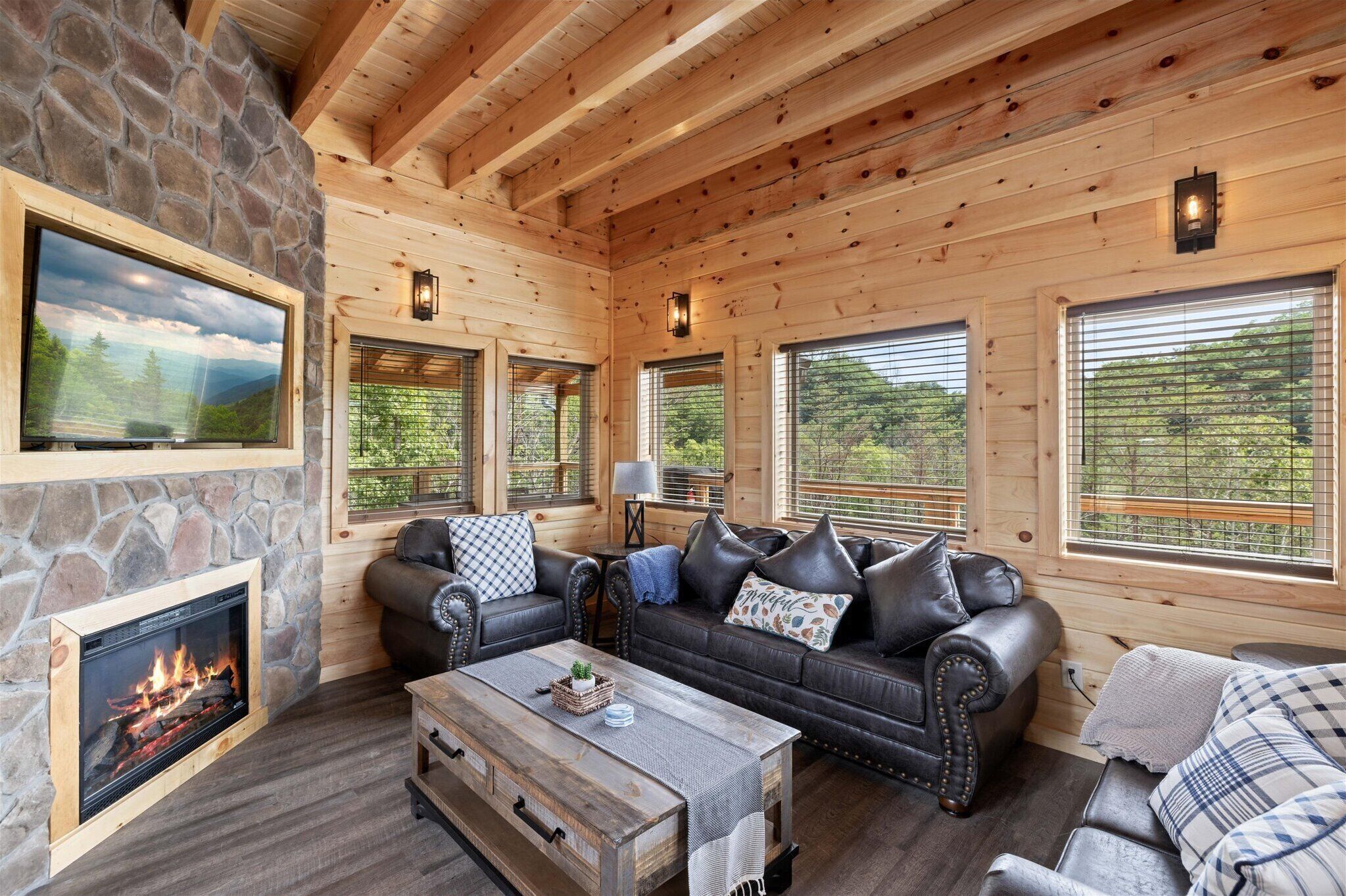 Ein gemütliches Blockhaus-Interieur mit Kamin aus Stein, Ledersofas und großen Fenstern mit Blick auf den umliegenden Wald.