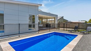 Una casa moderna con piscina, un patio cubierto y un patio trasero cercado.