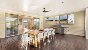 Un patio amplio con terraza de madera, mesa de comedor con sillas, una parrilla y un ventilador de techo.