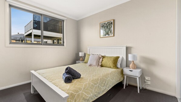 A bedroom with a bed, two bedside tables, a window, and a wall-mounted picture.