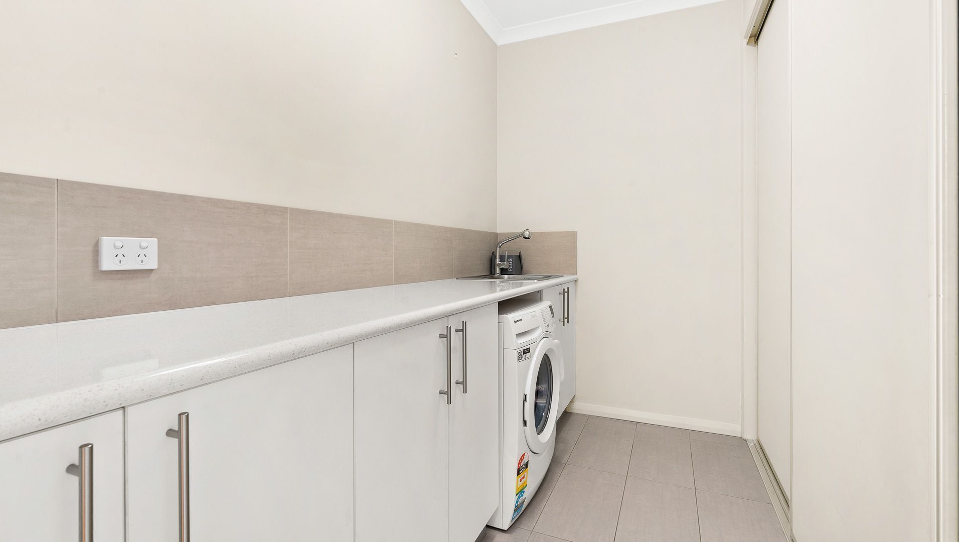 A laundry room with a washing machine, a sink, and a countertop.