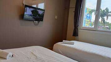 Ein Hotelzimmer mit zwei Betten, einem an der Wand befestigten Fernseher, einem Fenster mit Vorhängen und Blick auf Palmen.