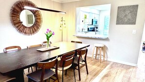 A dining area with a long table, chairs, a vase with flowers, a modern mirror, and a kitchen visible through an open door. - Spacious 3-Level Townhouse w/ 3 Community Pools, Tennis & Parking Pass for Rehoboth Beach (Rehoboth Beach)