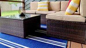 A wicker sofa with cushions and a striped pillow, a glass-top coffee table, and a blue striped rug. - Spacious 3-Level Townhouse w/ 3 Community Pools, Tennis & Parking Pass for Rehoboth Beach (Rehoboth Beach)