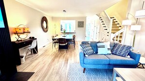 A modern living room with a blue sofa, a dining table, and a staircase. - Spacious 3-Level Townhouse w/ 3 Community Pools, Tennis & Parking Pass for Rehoboth Beach (Rehoboth Beach)