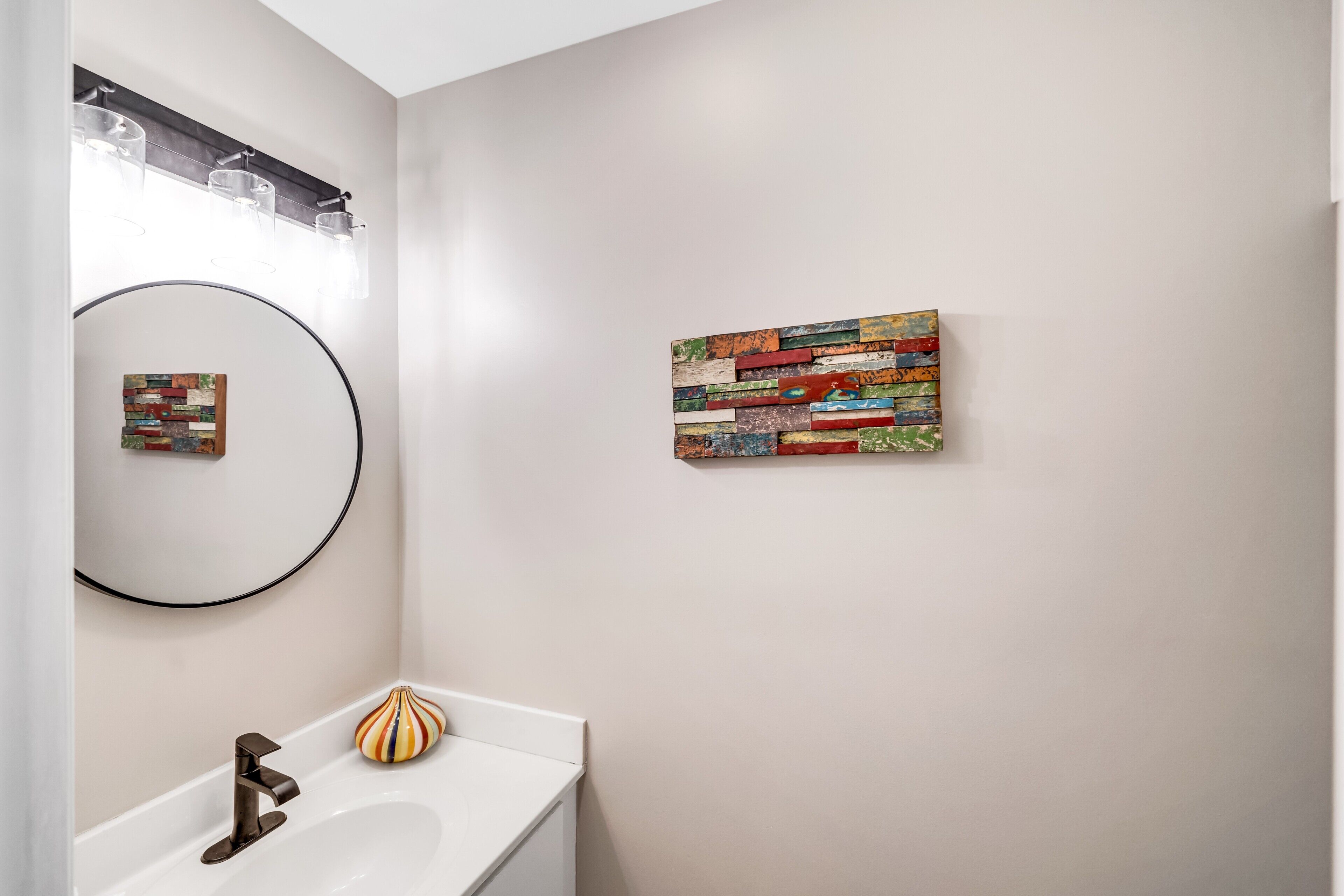 Een badkamer met een witte wasbak, een ronde spiegel en een kleurrijk abstract schilderij aan de muur.