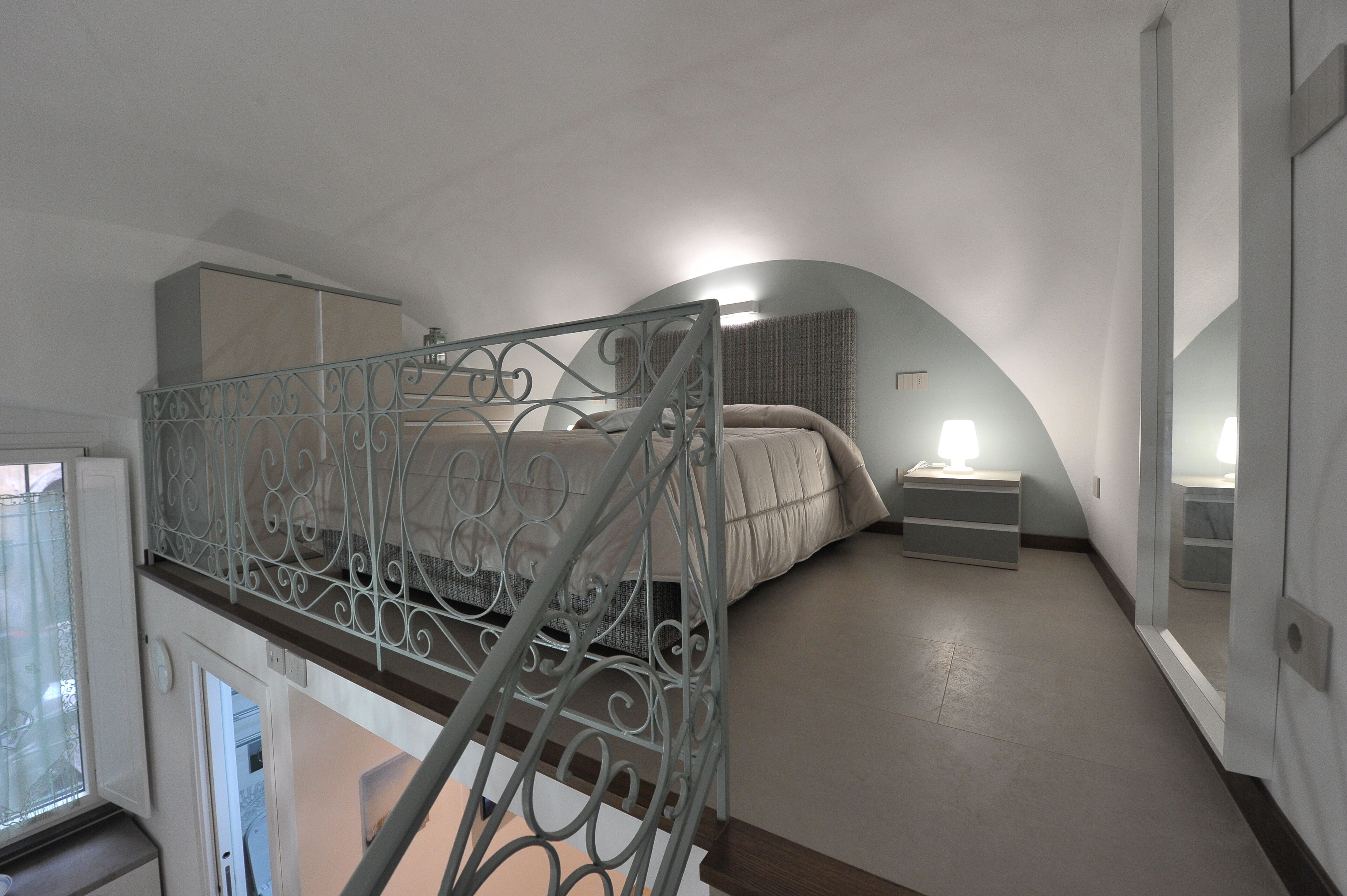 A bedroom with a curved ceiling, a bed with a headboard, a bedside table with a lamp, and a wardrobe.