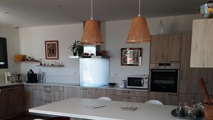 Moderni keittiö, jossa on keskellä sijaitseva saareke, valkoiset baarituolit, riippuvalaisimet ja puukehikoiset kaapit.