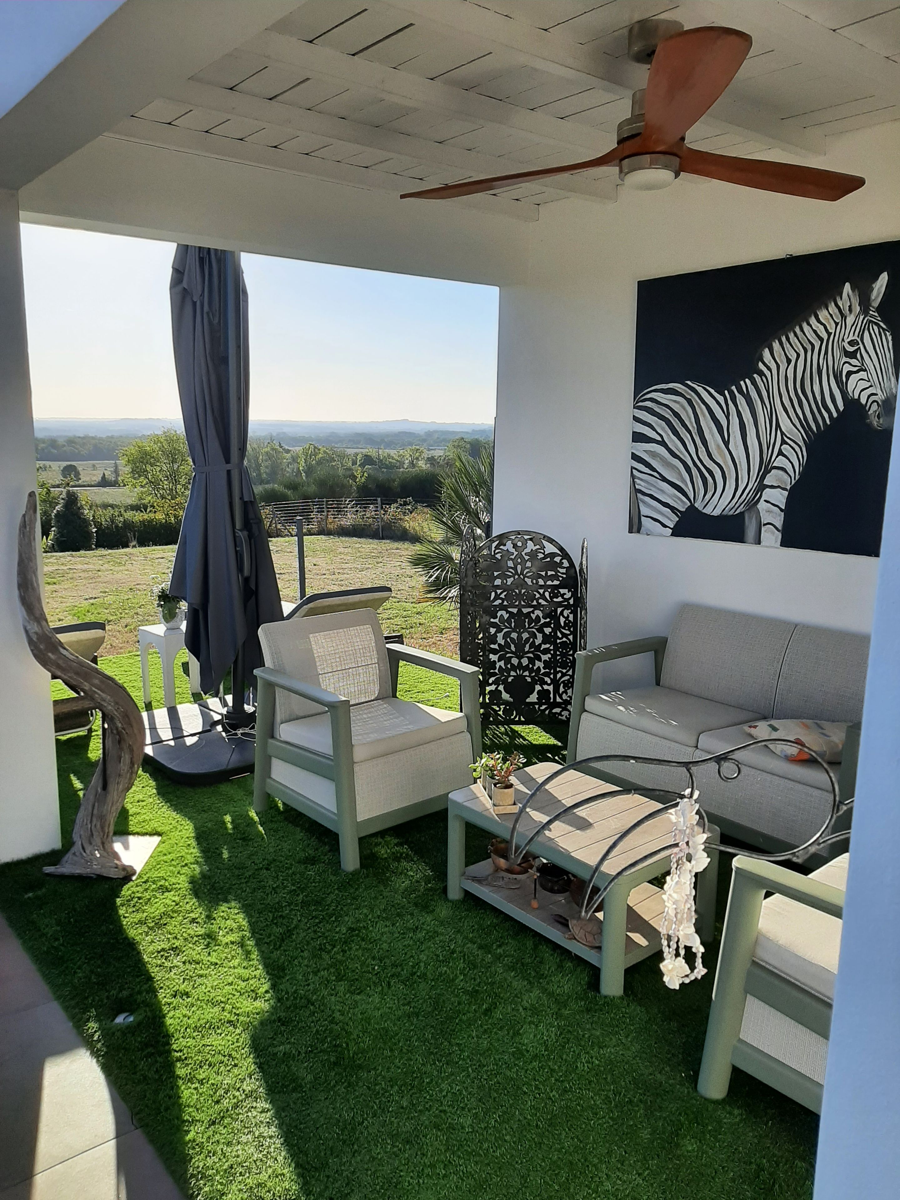 A room with a view of the countryside, a ceiling fan, a zebra painting, and a sofa.