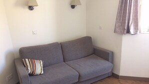 Un sofá gris con un cojín a rayas en una habitación con suelo de madera y dos lámparas fijadas a la pared.