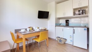 Una cocina compacta con una mesa de comedor, sillas, microondas, cafetera y un televisor en la pared.