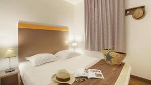 Una habitación de hotel con cama, lámparas de noche, un sombrero, gafas y una revista sobre la cama.