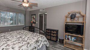 A bedroom with a bed, a ceiling fan, a bookshelf, and a window with blinds.