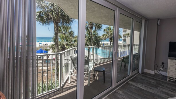 A balcony with a view of a beach, a pool, and palm trees.