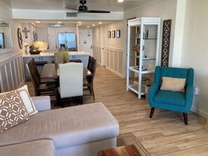 A modern living room with a sofa, teal armchair, and a dining area with a table and chairs.