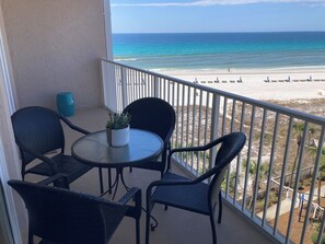 Un balcone con un tavolo rotondo e quattro sedie, vista su una spiaggia con alcune persone e ombrelloni.