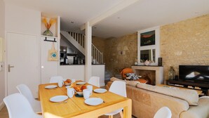 Una sala de estar moderna con una mesa de comedor de madera dispuesta para cuatro personas, un sofá color beige y una pared de piedra.
